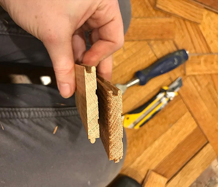Close up of two pieces of old hardwood flooring. The top edge of the groove on the piece on the left is almost completely worn away from sanding, compared to the piece on the right.