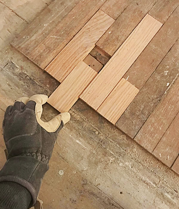 Sliding in new salvaged pieces of hardwood flooring.