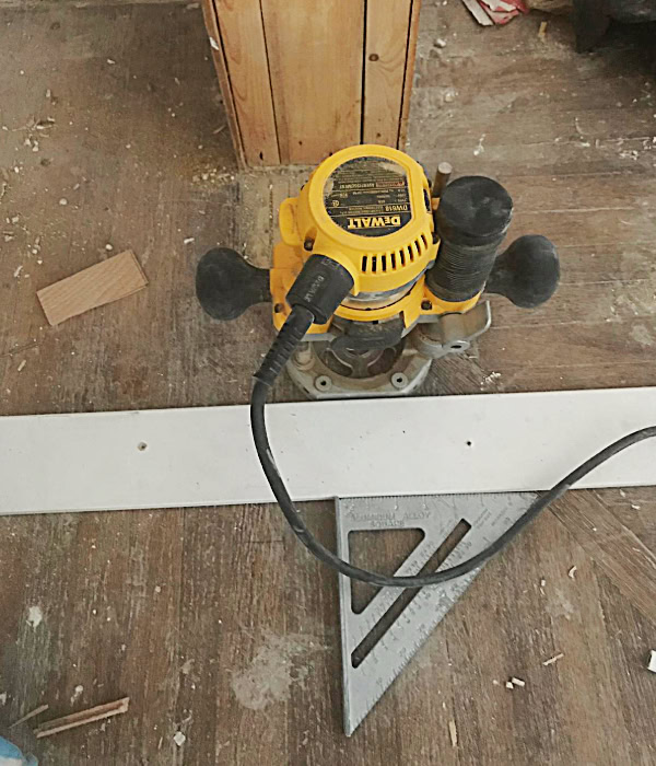 Using a router, a square and a straight edge to cut a finishing line in the flooring.