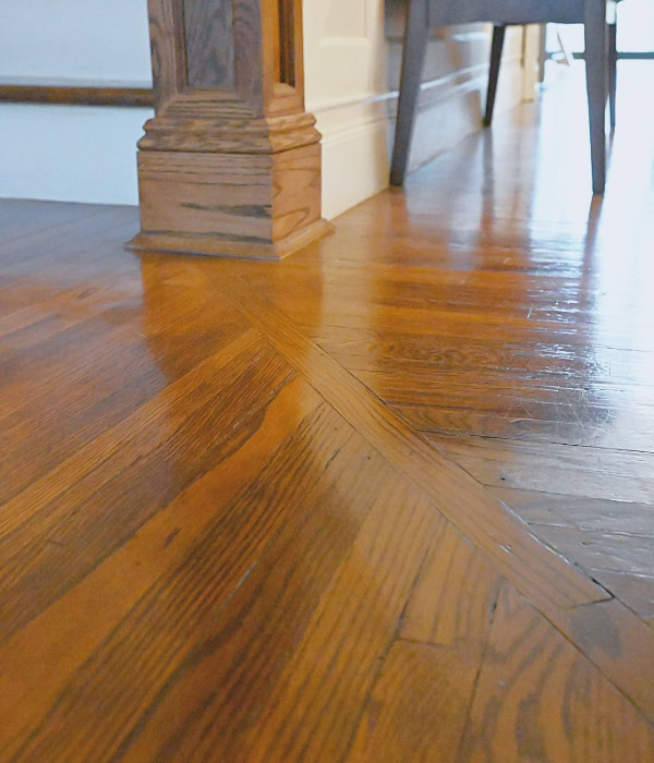 Close up of shining restored hardwood floors with diagonal character strip leading to staircase newel post