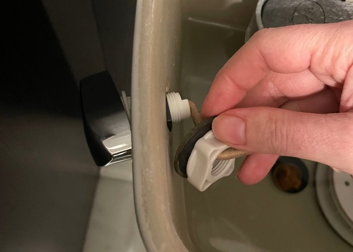 Replacing a toilet tank lever is an easy toilet upgrade. This is a photo of my hand taking off the threaded nut that holds on the toilet tank lever. 