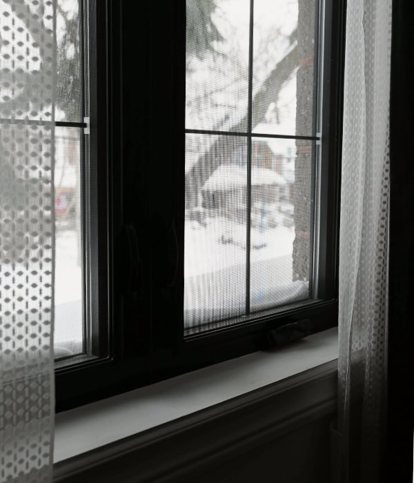 A close up of a bedroom window with black trim and white mesh drapes.