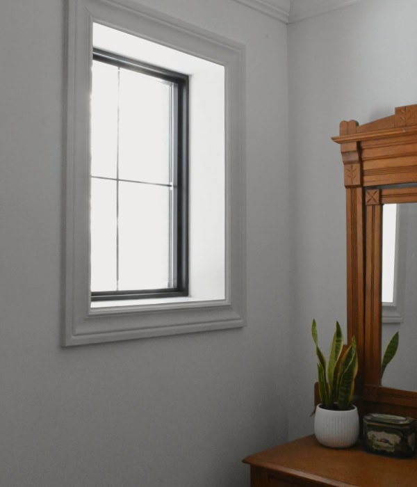 Wall after insulating a bedroom. Wall has a small square window with black trim. 