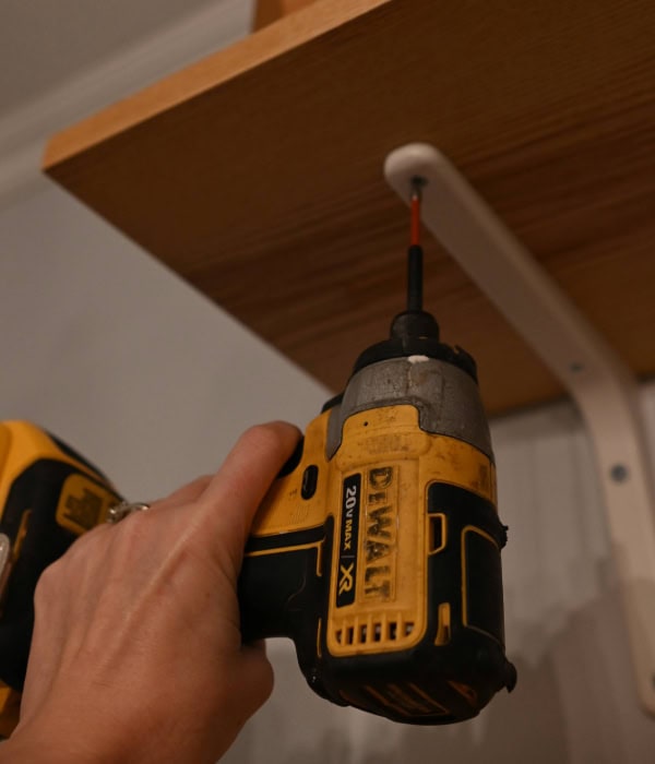 Close-up image of a Dewalt screwdriver attaching a shelf to the bracket to hang shelves on plaster walls.