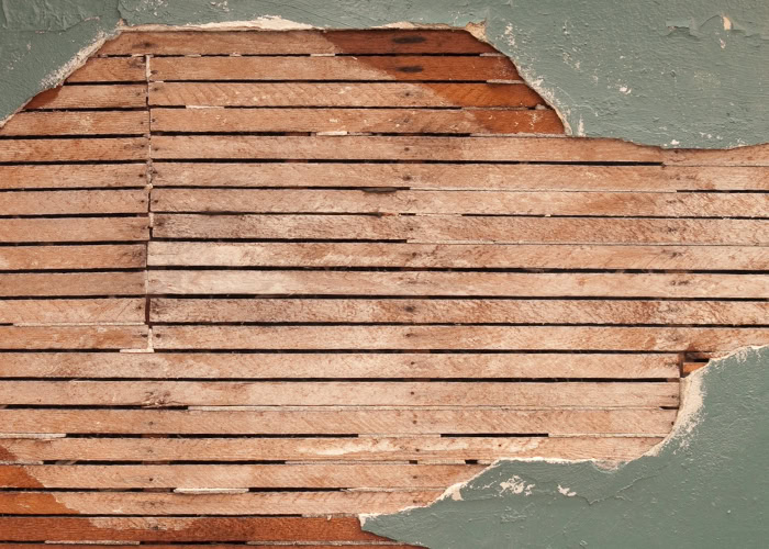 A lath and plaster wall with some plaster cracked off to reveal the lath underneath.