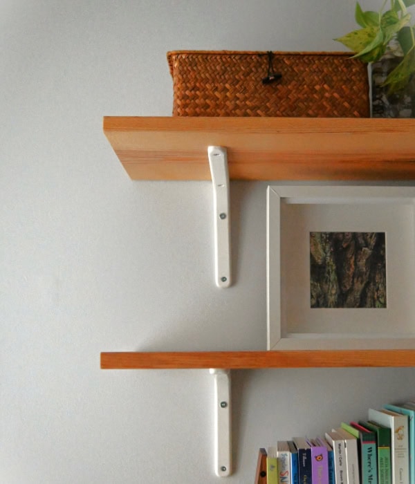 Wooden shelves with a woven glass box, children's books and a picture of a tree bark on wall shelves hung on plaster walls