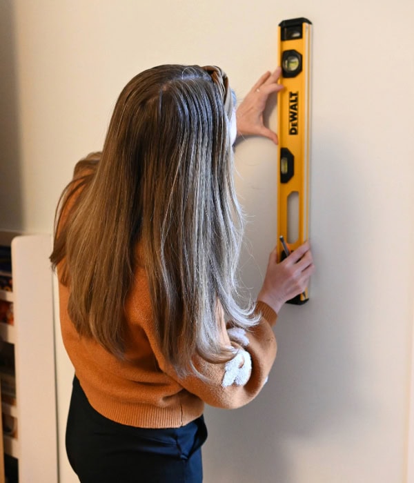 A woman using a level, holding it up against the wall, preparing to hang shelves on plaster walls. 